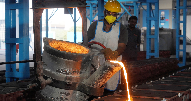 A worker cautiously transfers pours molten metal into a substantial metal container with precision and caution.