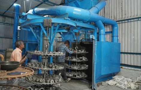 A pair of men are seen diligently operating a metal ring manufacturing apparatus to create the desired products.