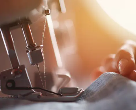 An individual is engaged in the art of sewing, using sewing machine to create intricate stitches on fabric with focus.