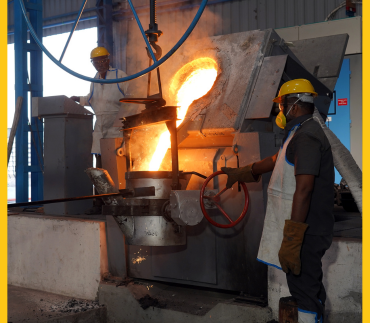 A worker cautiously transfers pours molten metal into a substantial metal container with precision and caution
